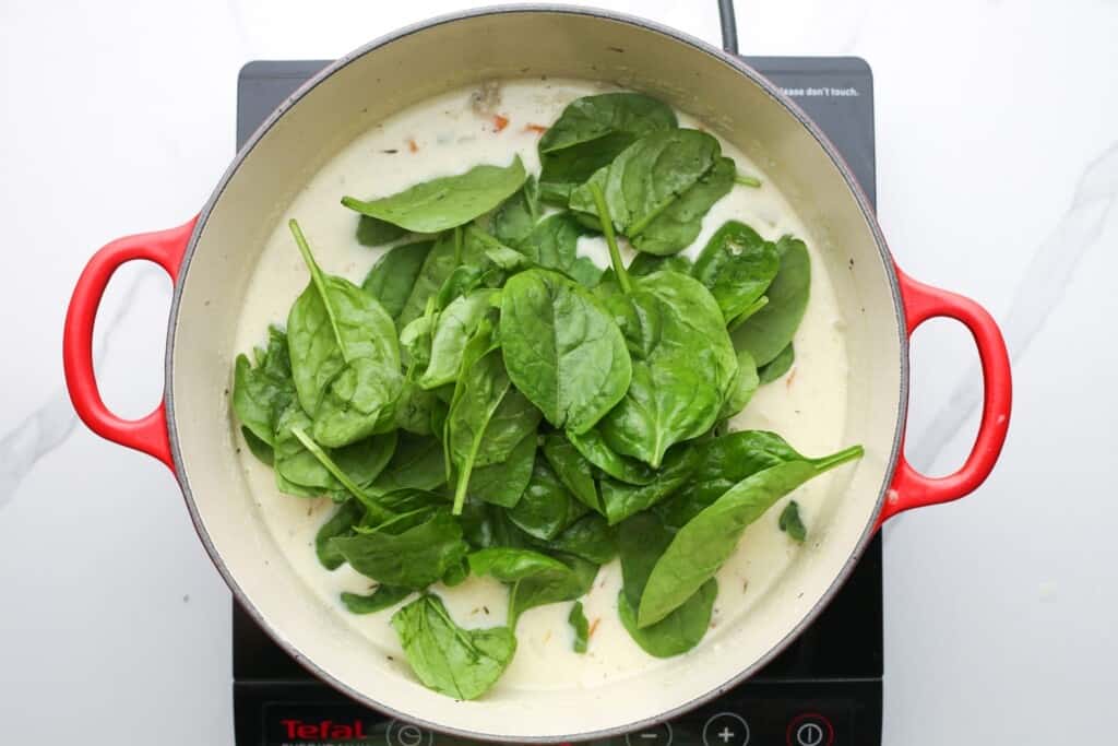 baby spinach added to a pot of creamy soup.