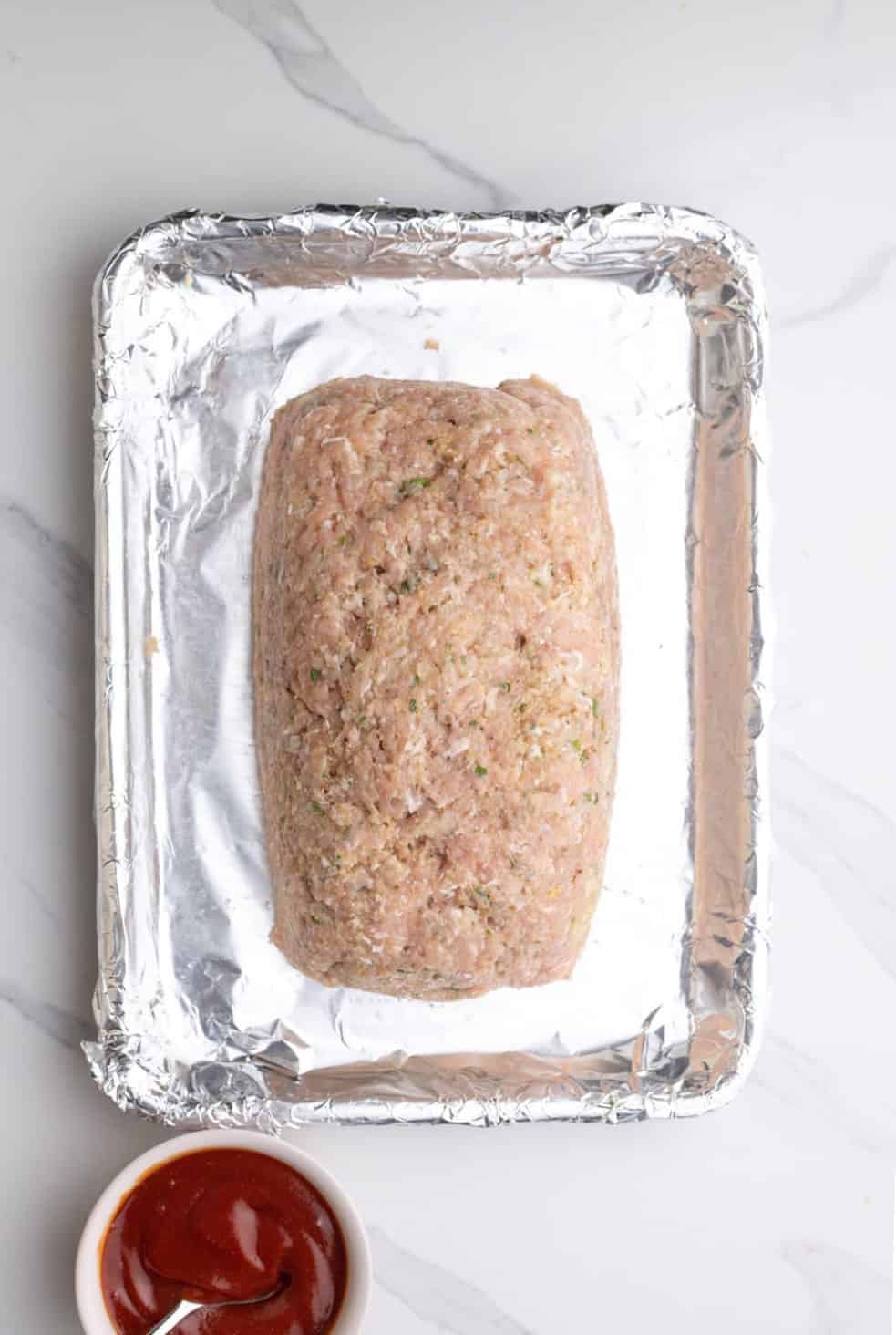 a meatloaf made with ground chicken on a sheet pan lined with foil.