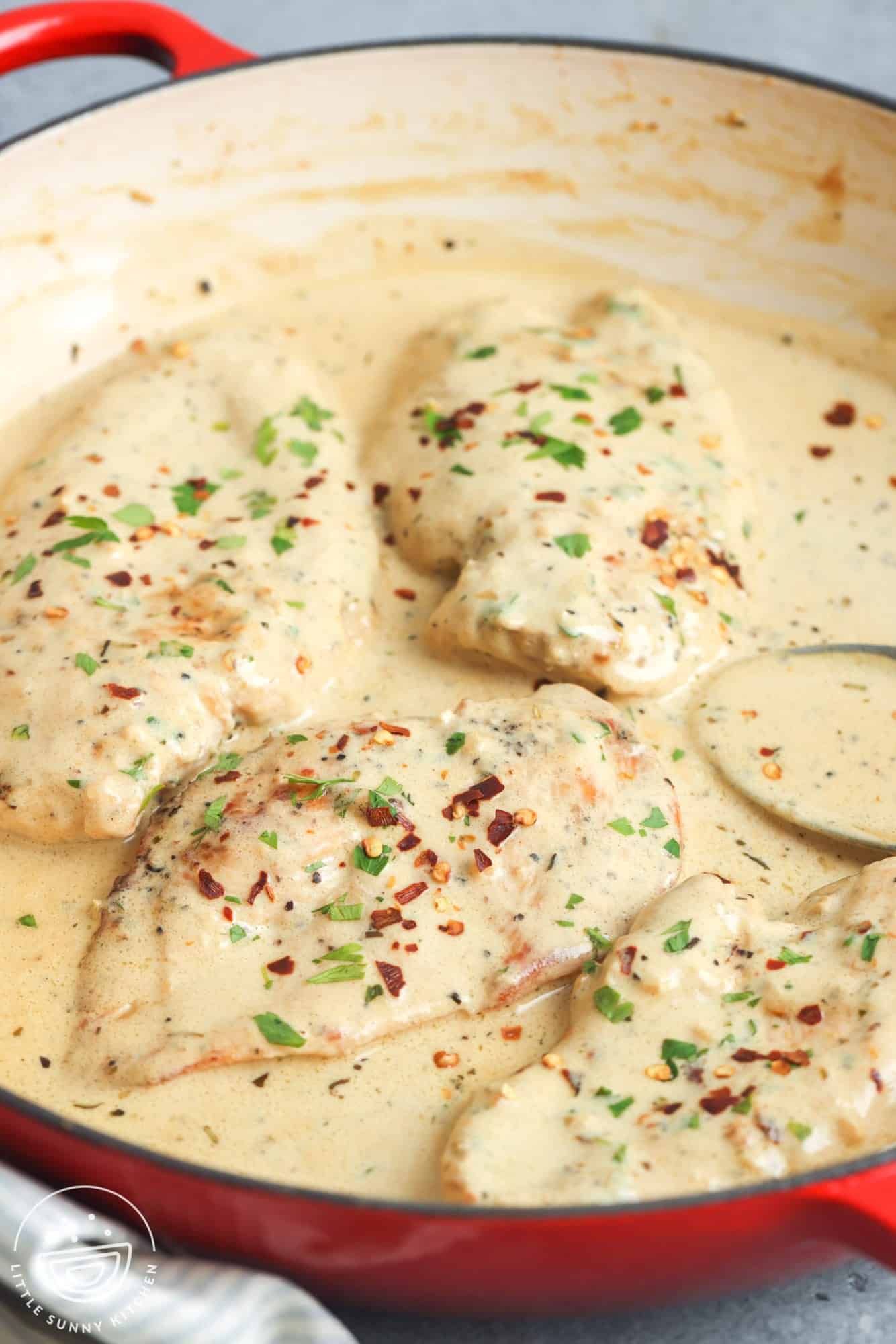 a skillet of cream cheese chicken breasts with crushed red peppers and herbs. 