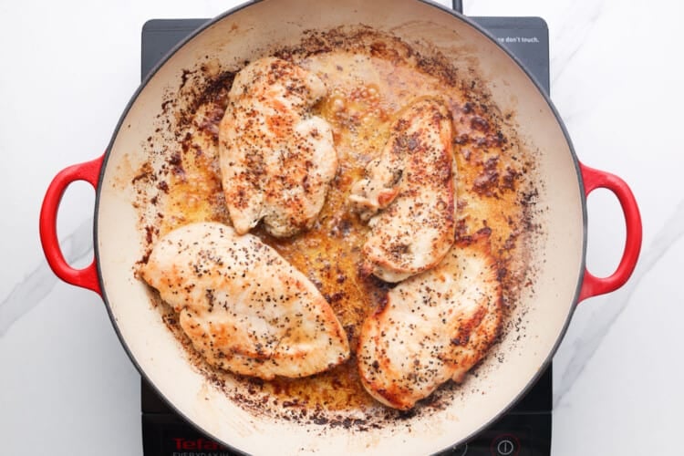 Seared chicken breasts in a skillet on a stove top.