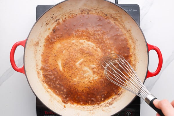 A hand stirring a sauce in a pan with a whisk.