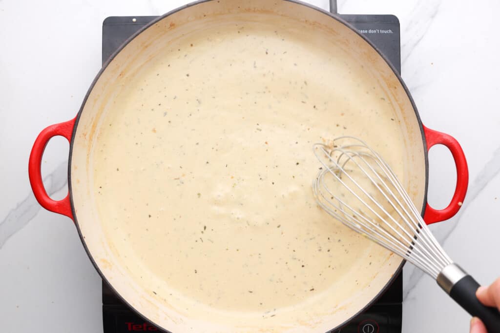 a pan of cream cheese sauce with a whisk. 