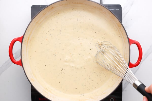 A hand whisking a pot of white sauce.