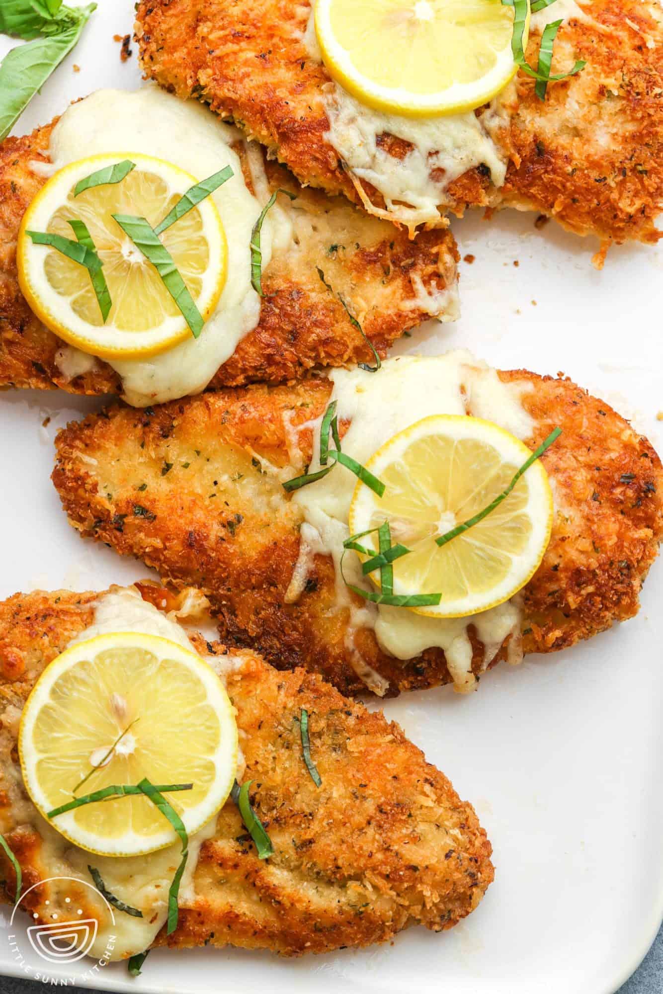 a platter of crispy chicken romano cutlets topped with lemon and herbs.