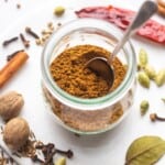Homemade garam masala blend in a small Weck jar with a small spoon, and whole spices on the sides.