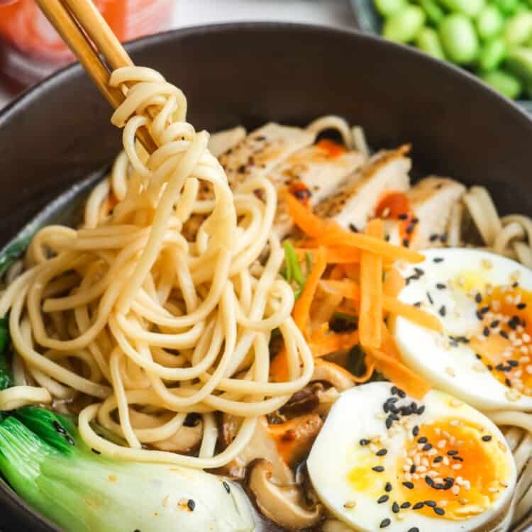 chopsticks picking up noodles from a bowl of homemade ramen with eggs and bok choi