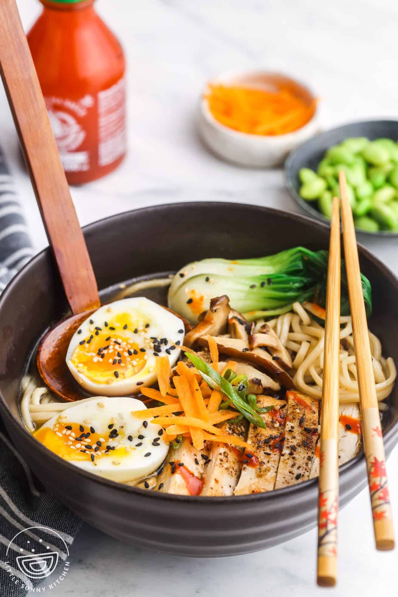 a black bowl of ramen with chicken, eggs, and veggies. A set of chopsticks is on the bowl.
