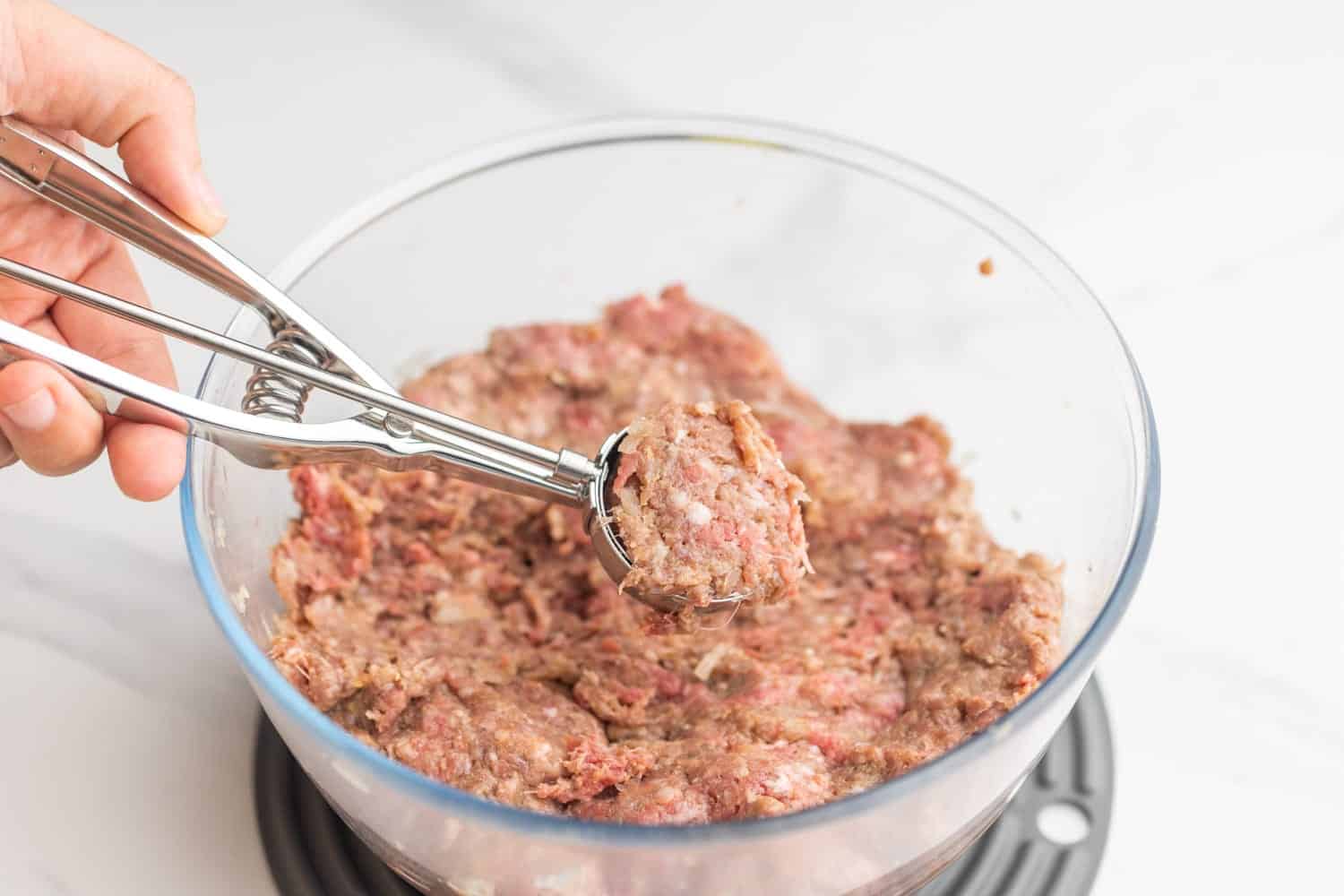 a hand using a cookie scoop to portion out meat for swedish meatballs