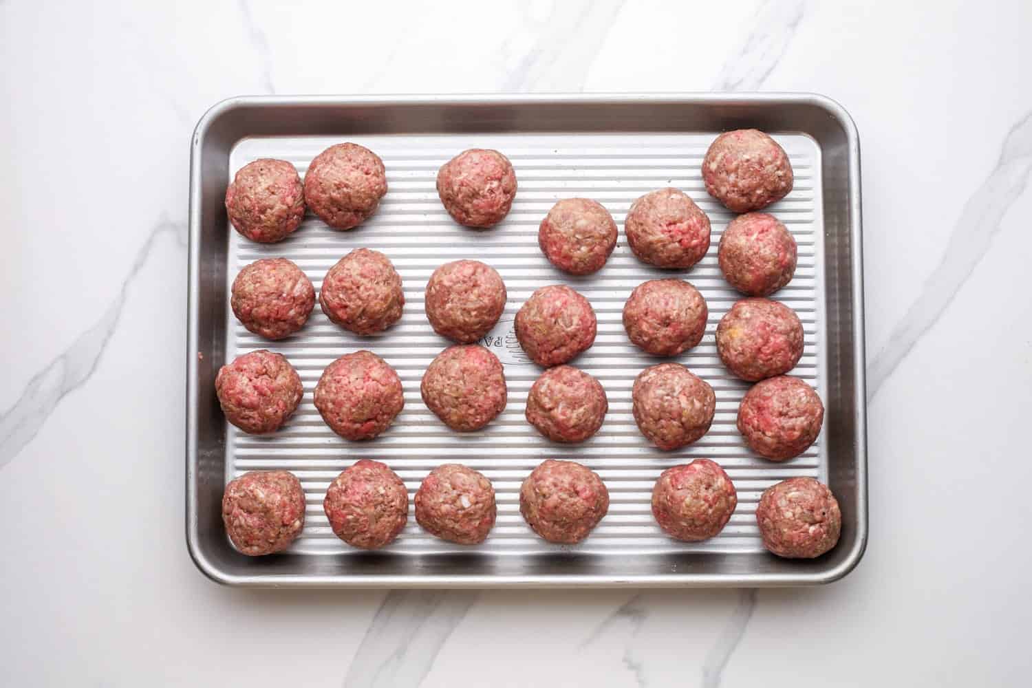 Meatballs formed and arranged on a sheet pan.