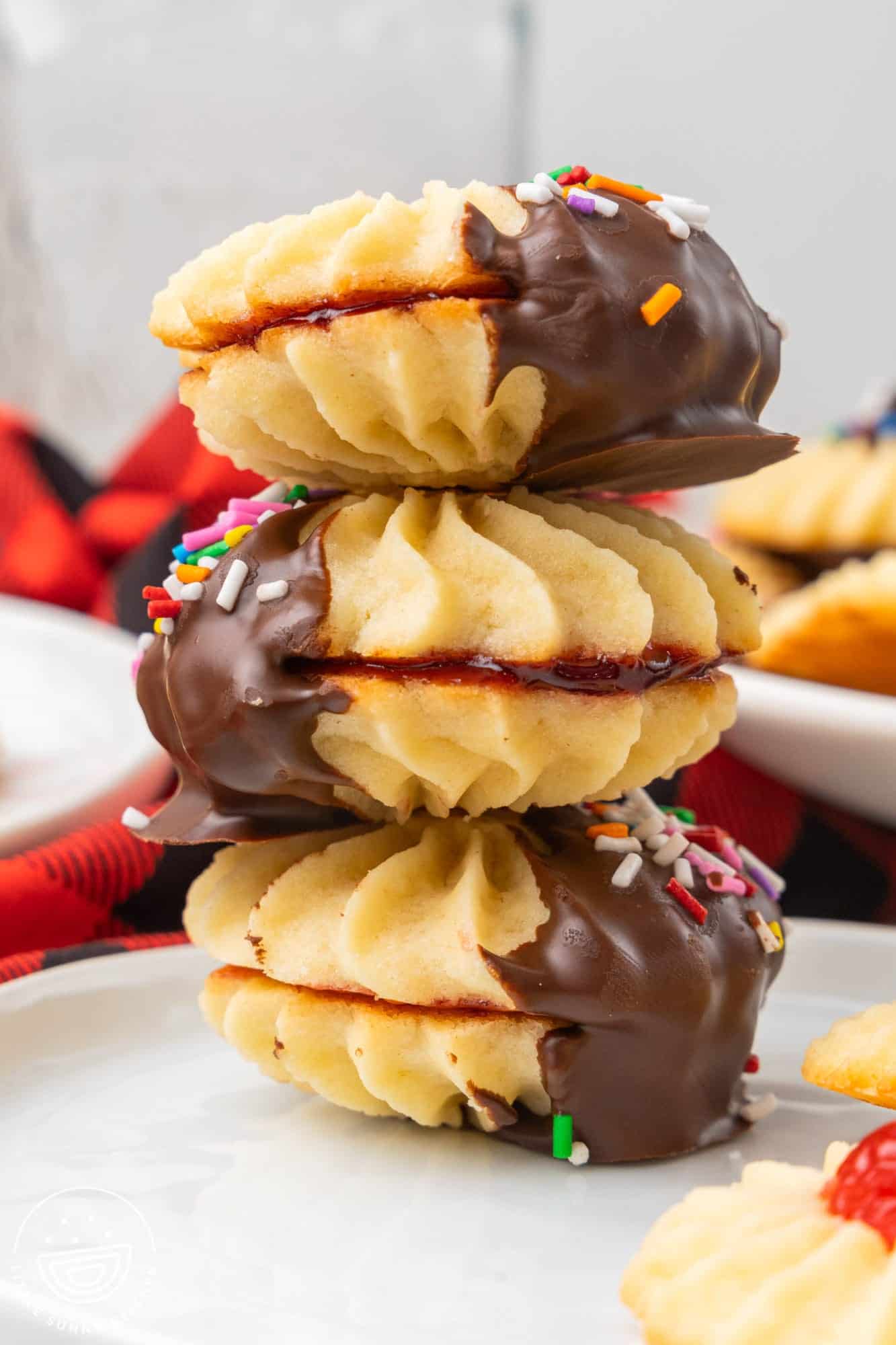 three italian butter cookie sandwiches with jam in the center and the ends dipped in chocolate. Cookies are stacked on top of each other and viewed from the side.