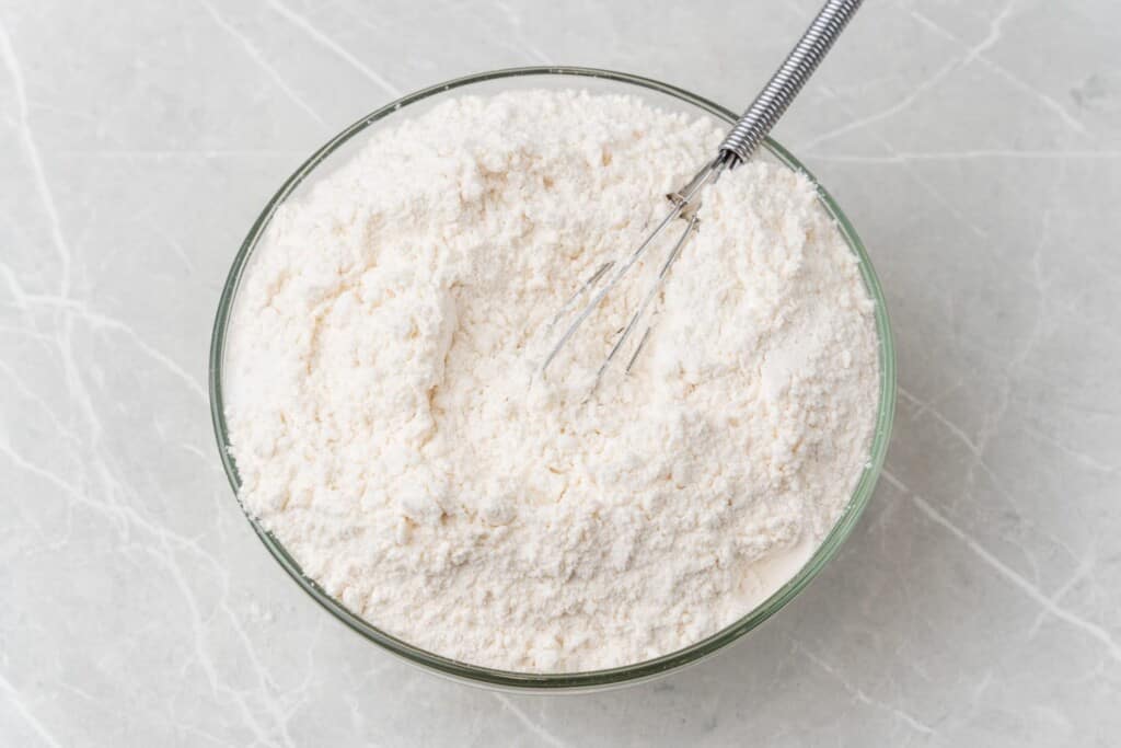 a bowl of flour with a whisk,