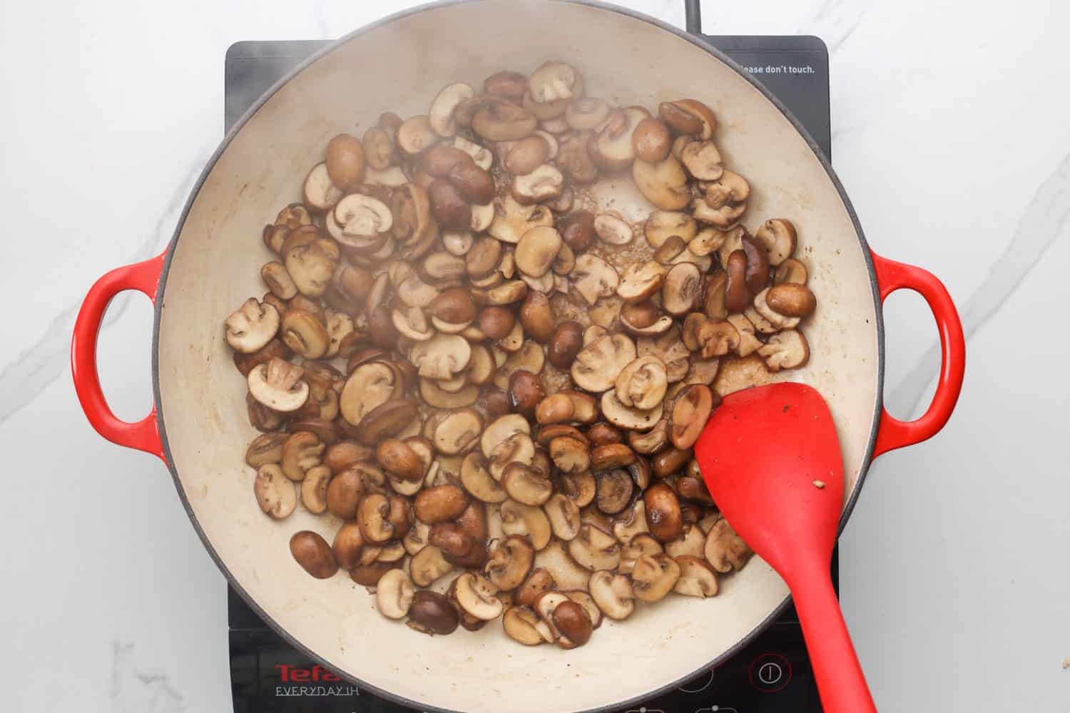 Mushrooms being cooked in a skillet, and a red spatula