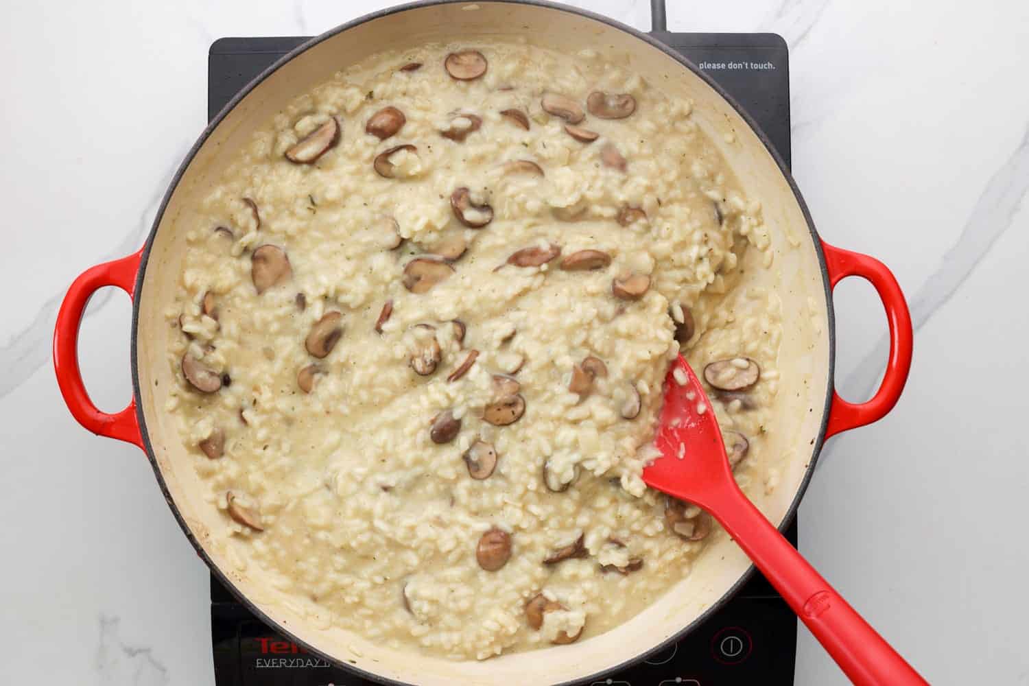 Cooked mushroom risotto in a pan with a silicone spatula