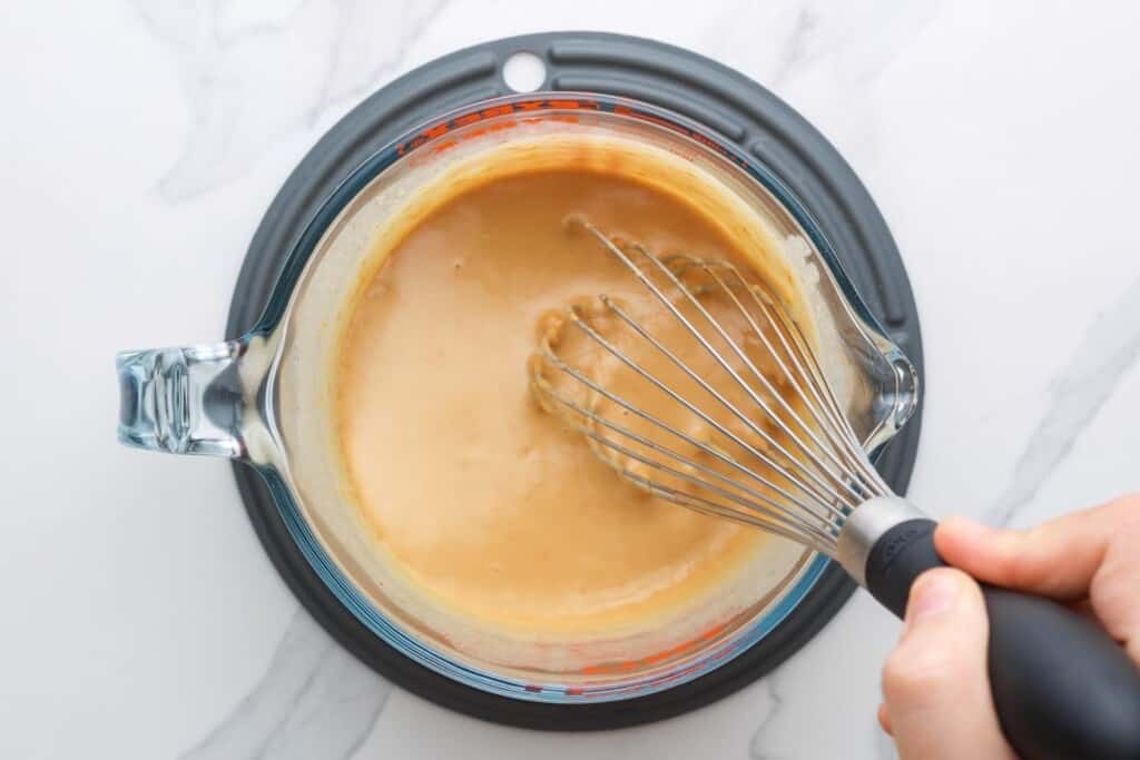 peanut sauce in a measuring cup, mixed with a whisk.