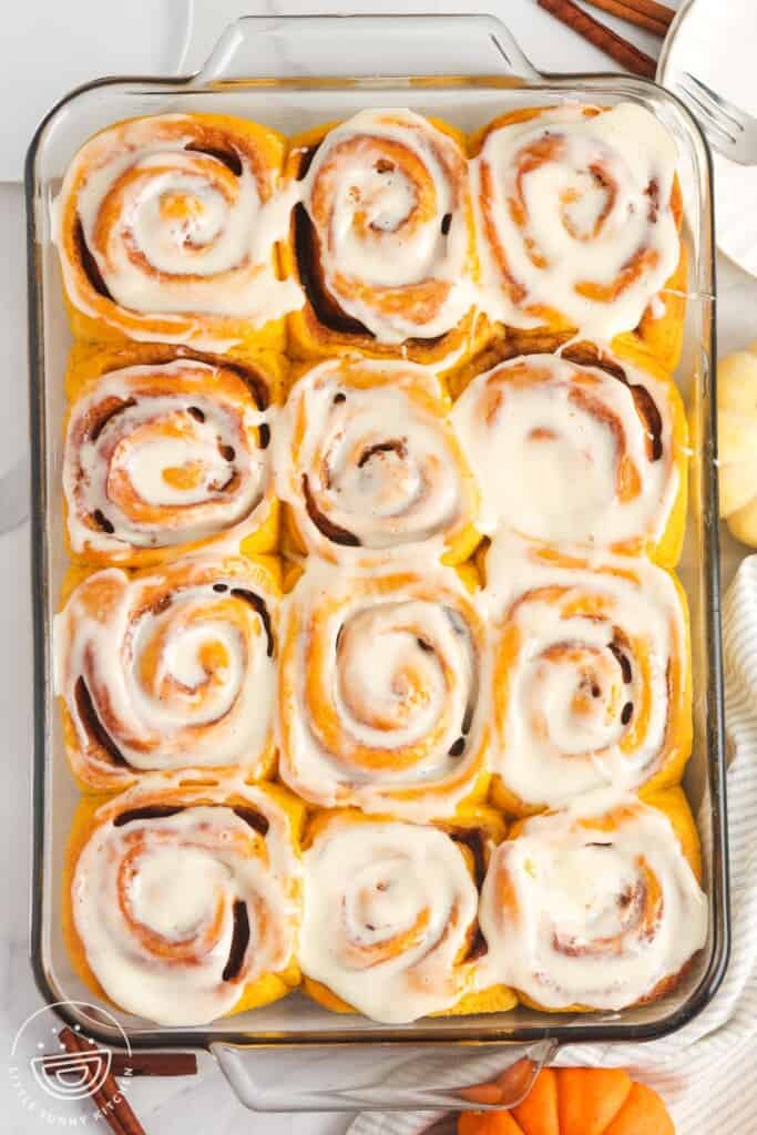 a 9x13 glass baking dish with 12 pumpkin cinnamon rolls, covered in icing.