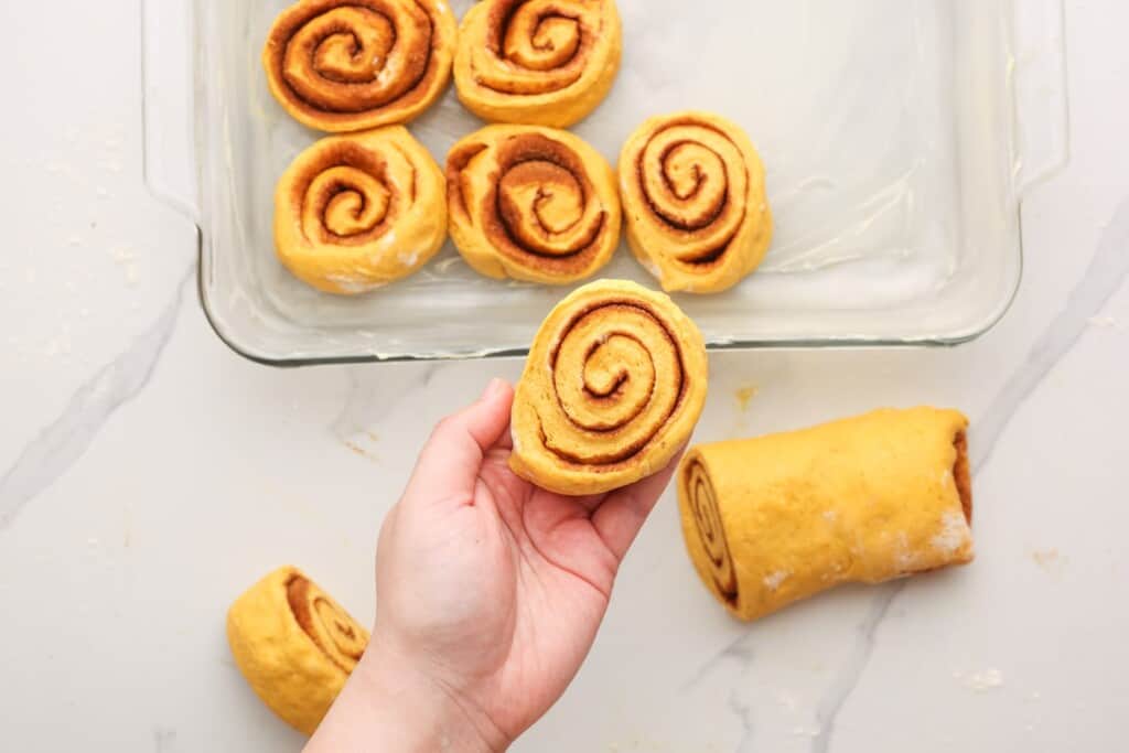 sliced pumpkin cinnamon rolls, uncooked, added to a buttered pan.