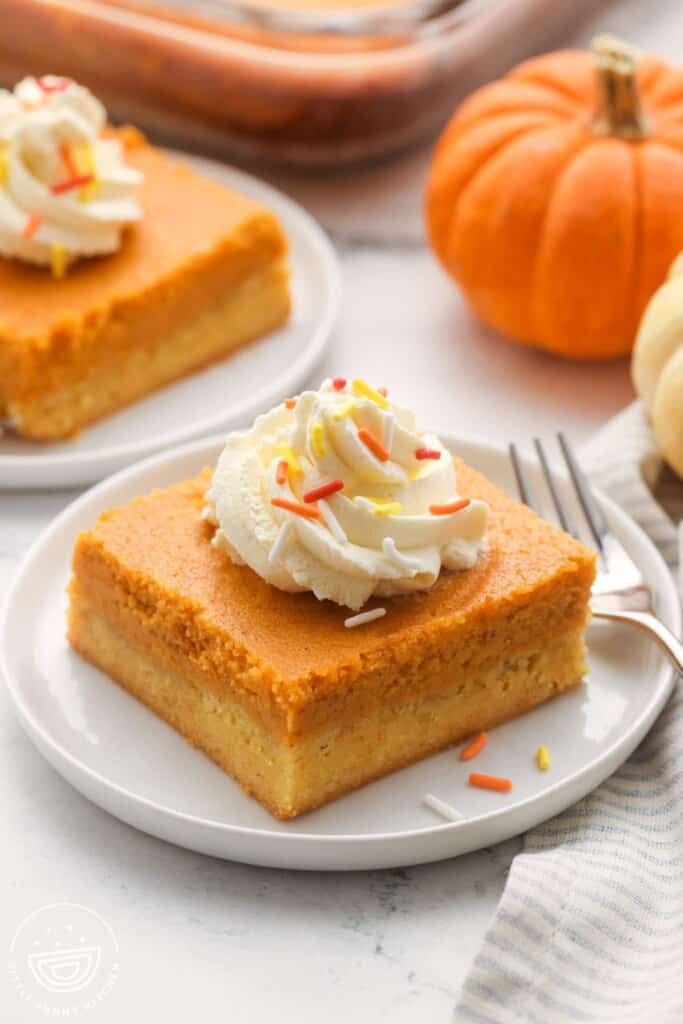 a square slices of pumpkin gooey butter cake topped with whipped cream and sprinkles.