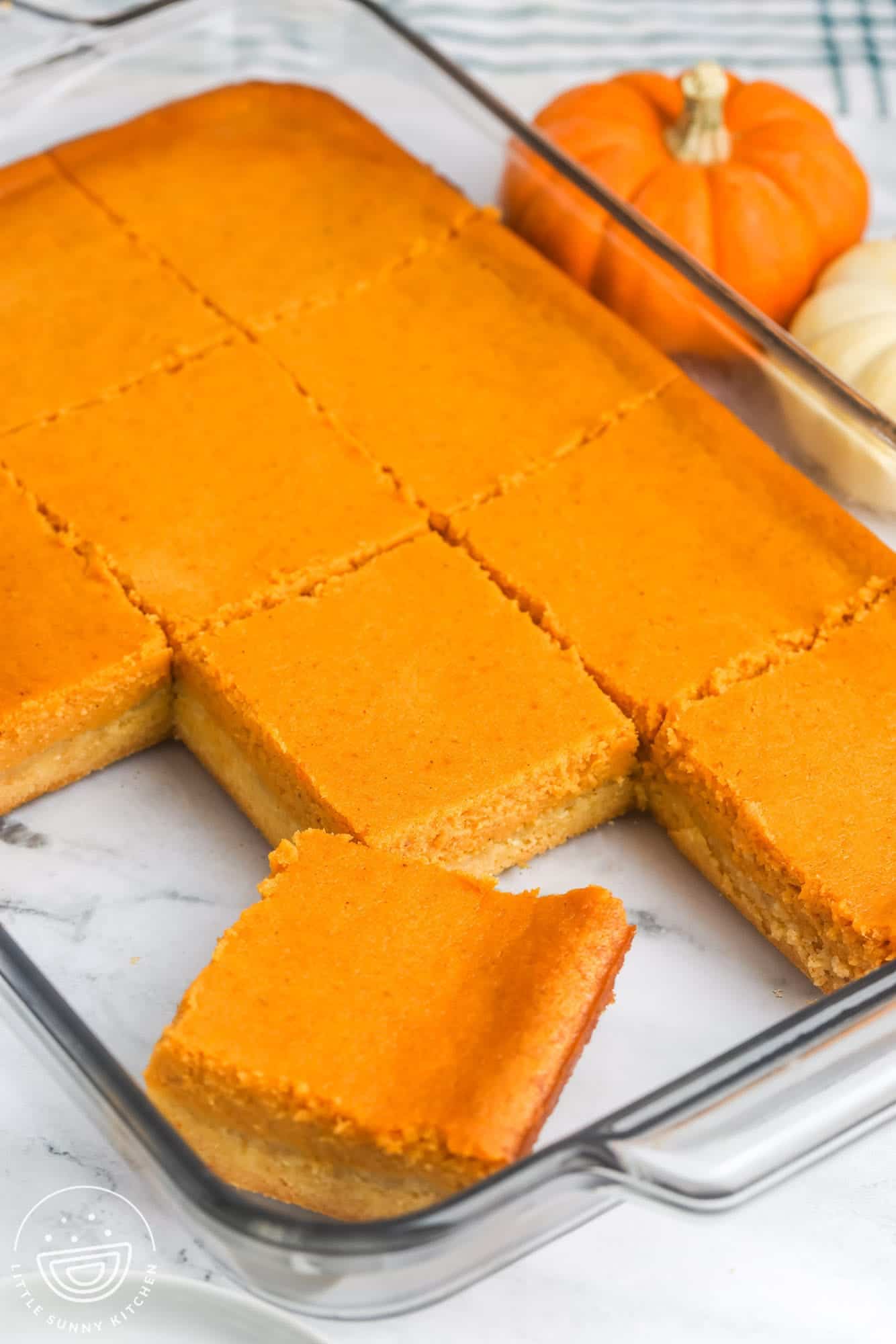 a clear glass pan of pumpkin gooey butter cake cut into squares
