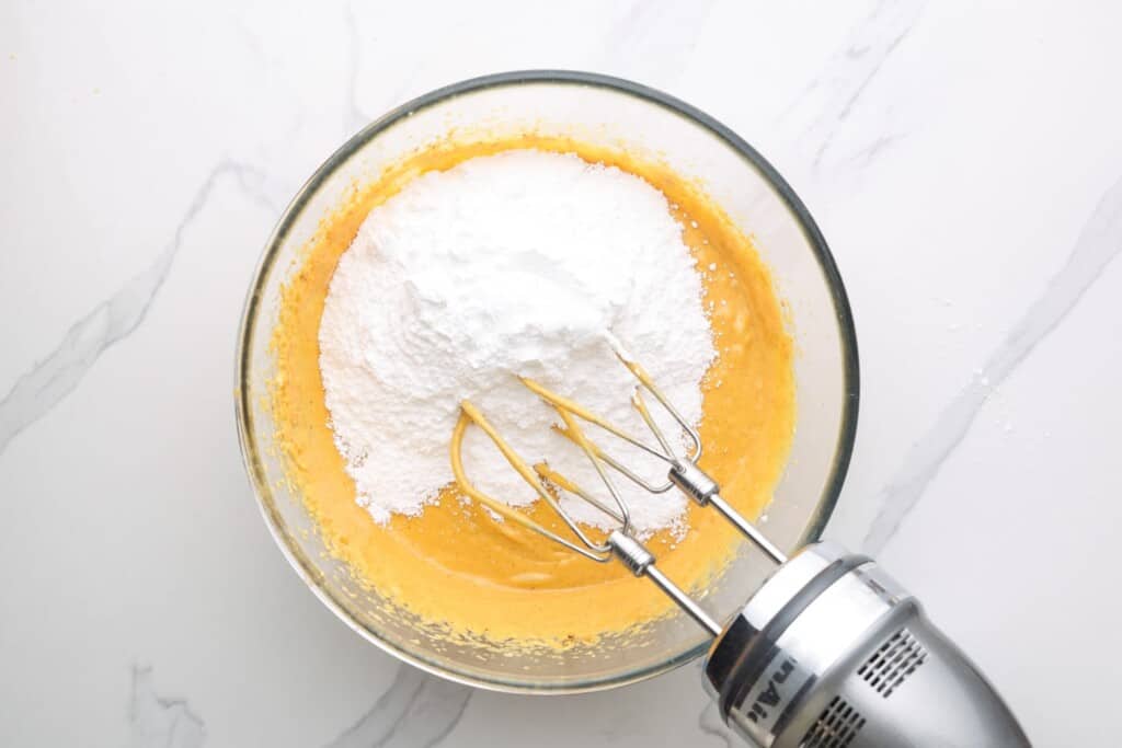 powdered sugar added to pumpkin cream cheese mixture with a silver hand mixer.