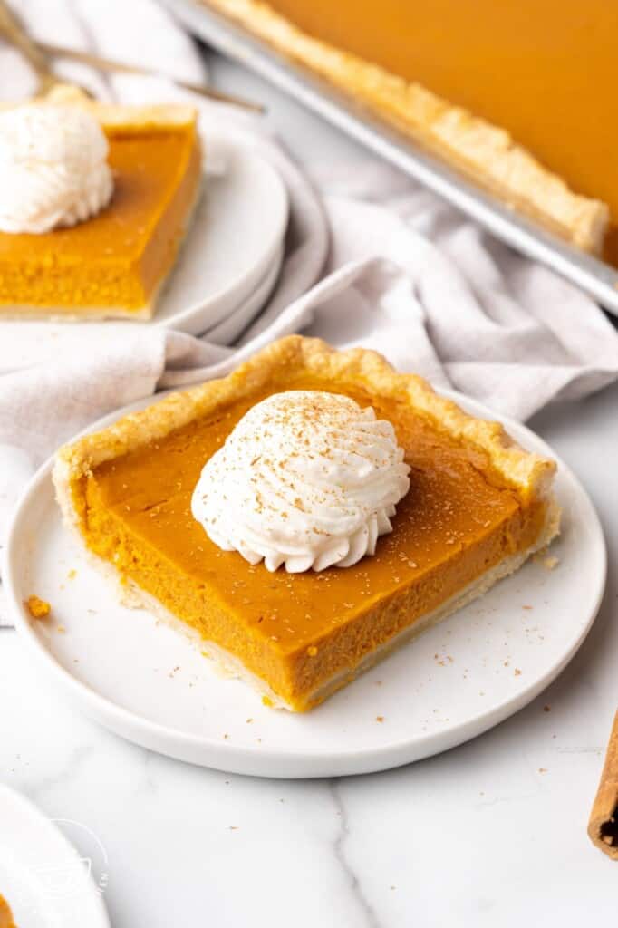 a square piece of pumpkin slab pie topped with whipped cream, on a white plate.