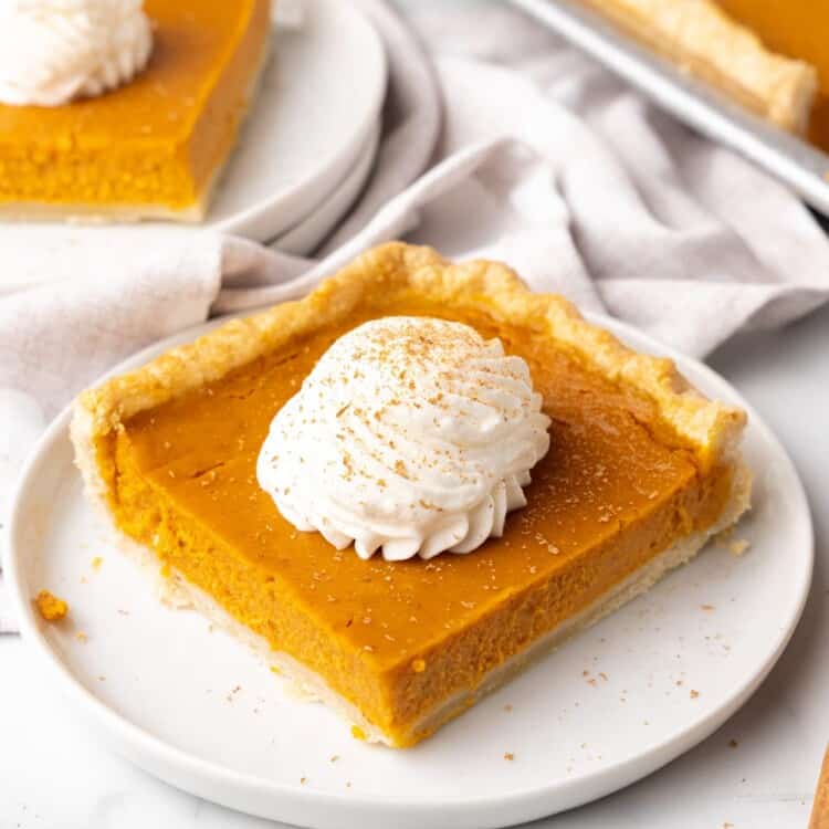 a square piece of pumpkin slab pie topped with whipped cream, on a white plate.