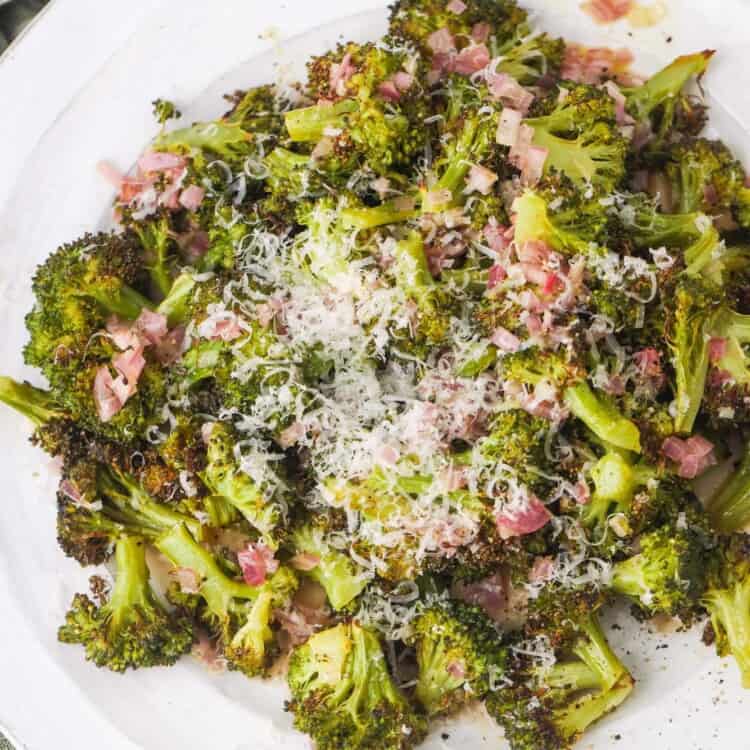 Overhead shot of roasted broccoli on a large plate and small dice shallots, sprinkled with grated parmesan.