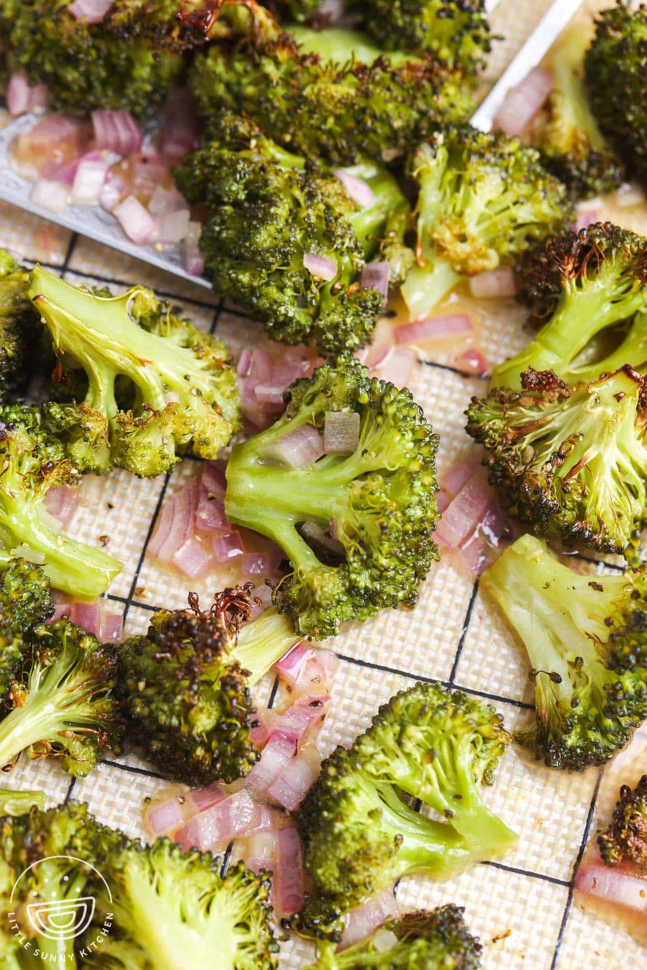 Roasted broccoli on a sheet pan with silicone mat, and some shallots shown from the vinaigrette