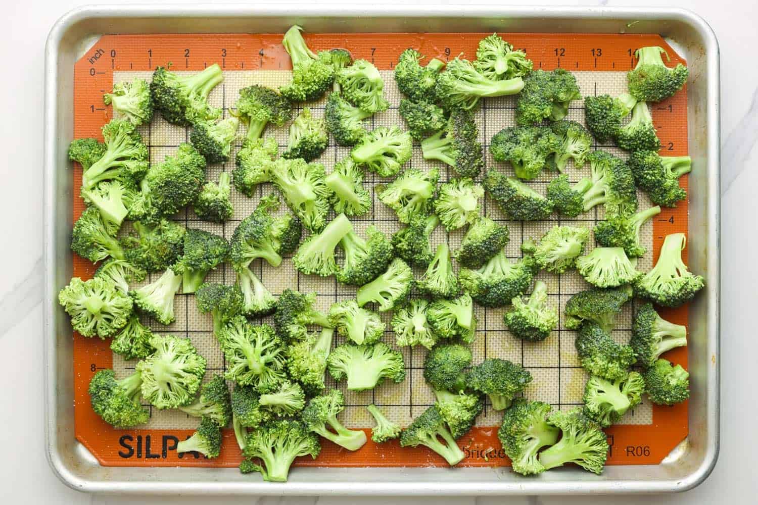 Broccoli florets with olive oil on a sheet pan lined with a silicone mat