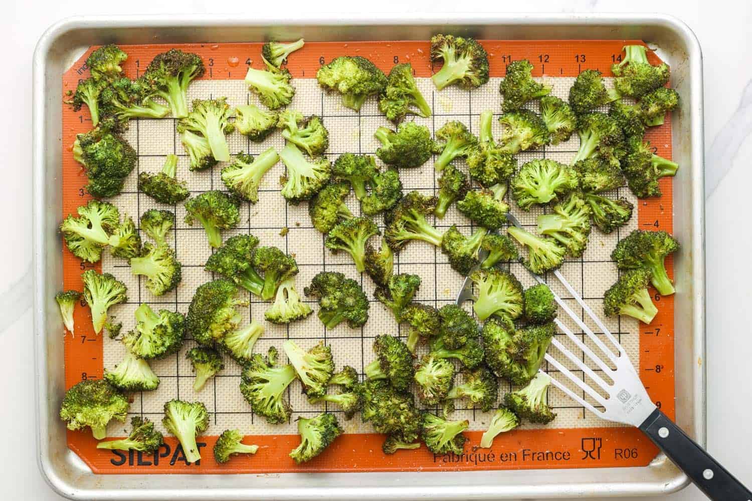 Roasted Broccoli florets with a fish spatula for turning on a sheet pan lined with a silicone mat