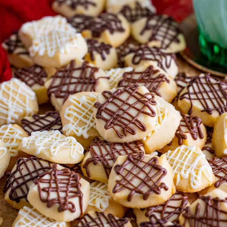 a pile of chocolate drizzled shortbread bites on a red tablecloth.