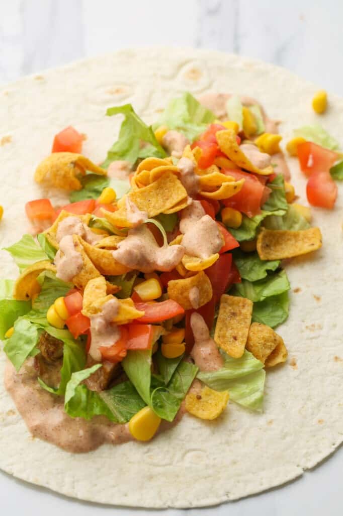 A tortilla topped with chicken, lettuce, tomatoes, sauce, and chips.
