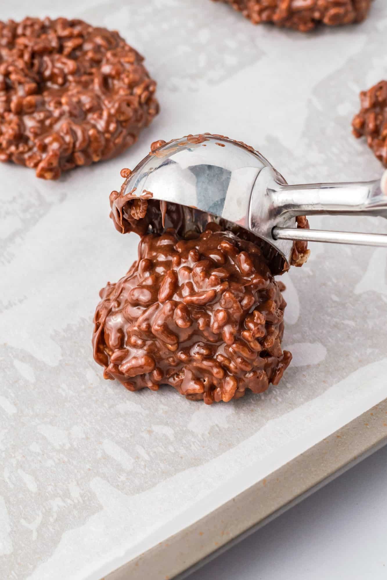 rice krispie cookies added to a pan with a large cookie scoop.
