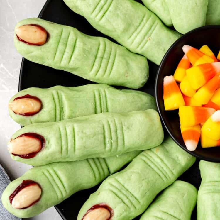 a platter of green witch finger cookies with a bowl of candy corn in the center.