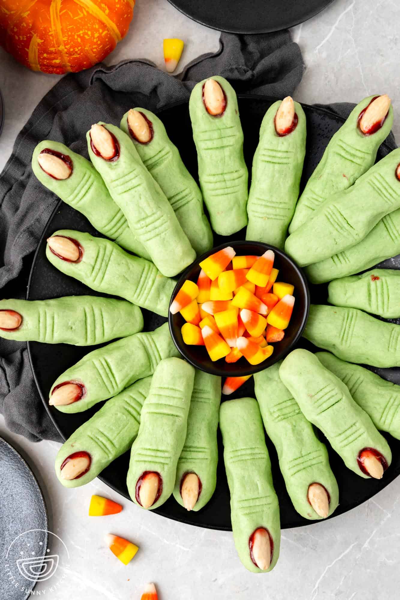 witch fingers arranged on a round platter in a circle. a bowl of candy corn is in the center.