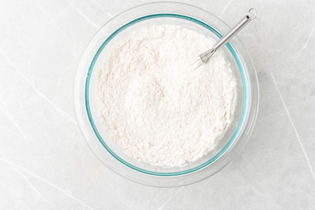 a bowl of flour with a whisk in it.