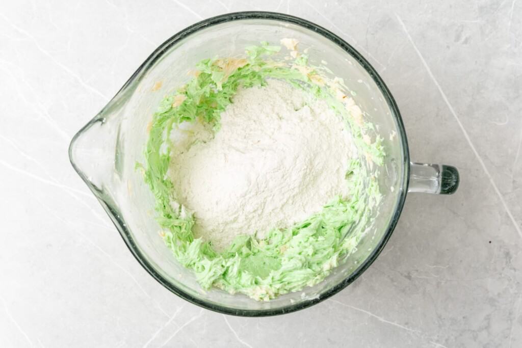 Flour added to green cookie dough in a large glass bowl.