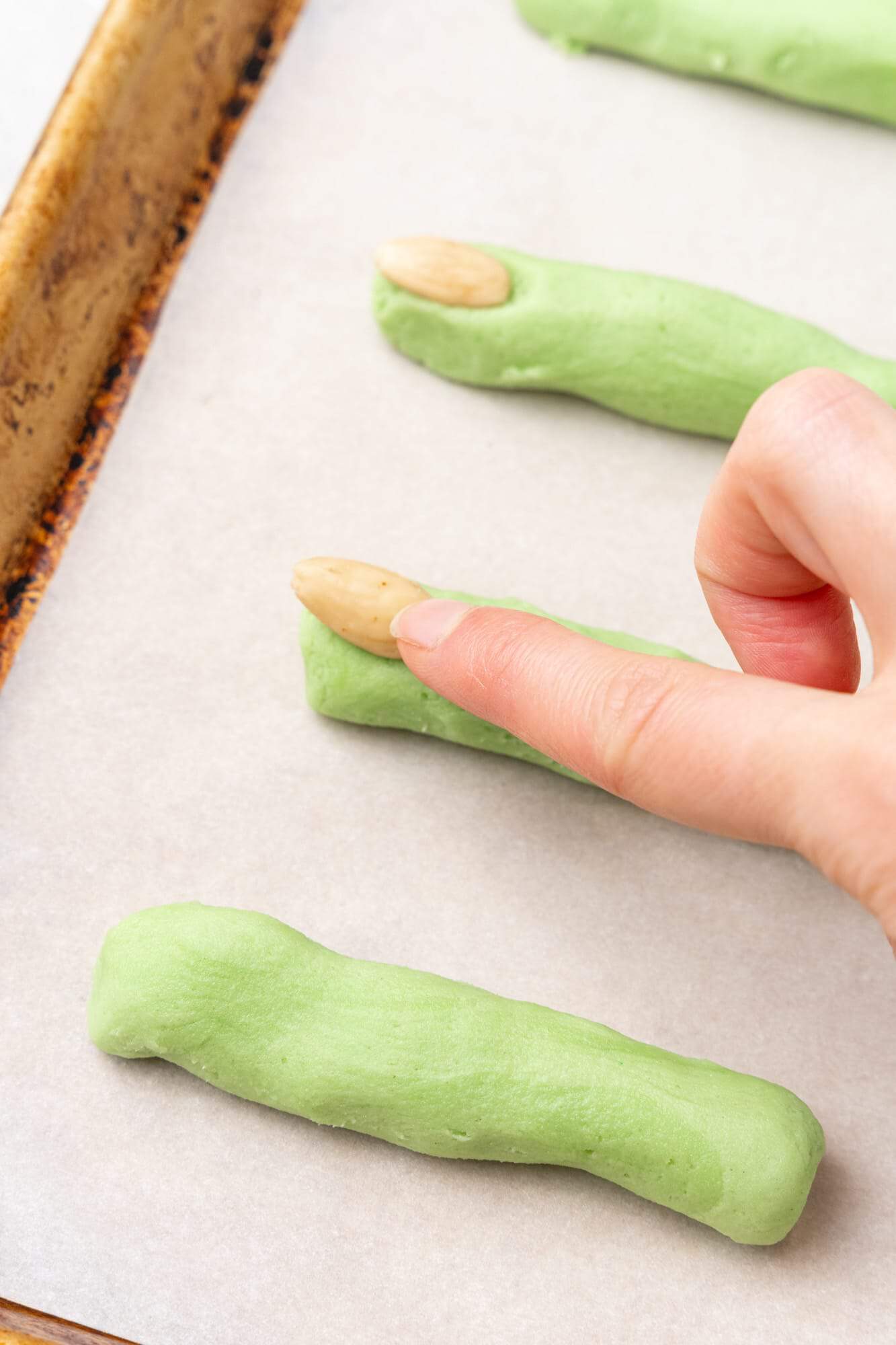 finger shaped cookies on a tray. almonds are pressed into the cookies to create witch fingernails.