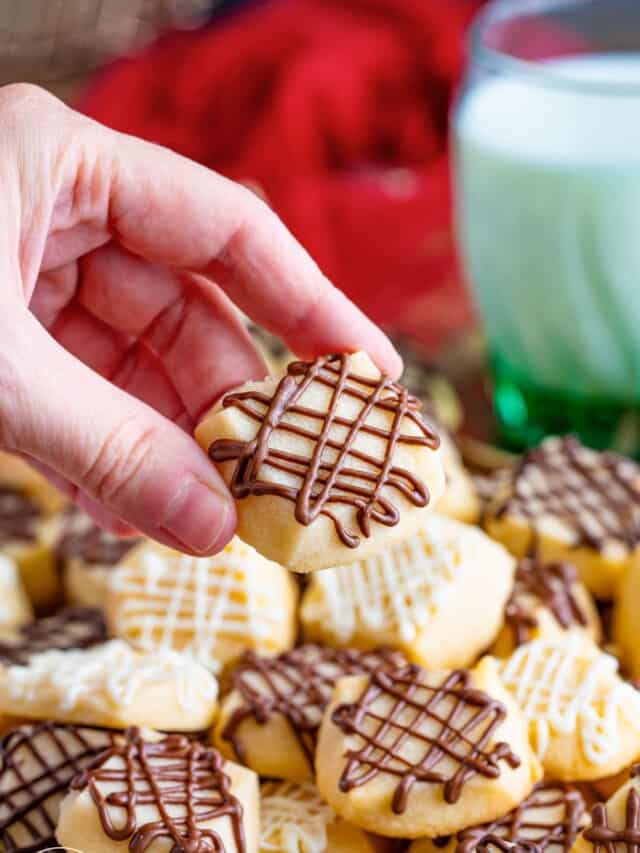 a hand holding a shortbread cookie with chocolate drizzled on top.