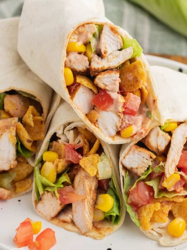 two chicken wraps, cut in half, on a plate. Inside of the wrap sandwiches is chicken, corn, tomatoes, lettuce, cheese, and fritos corn chips.