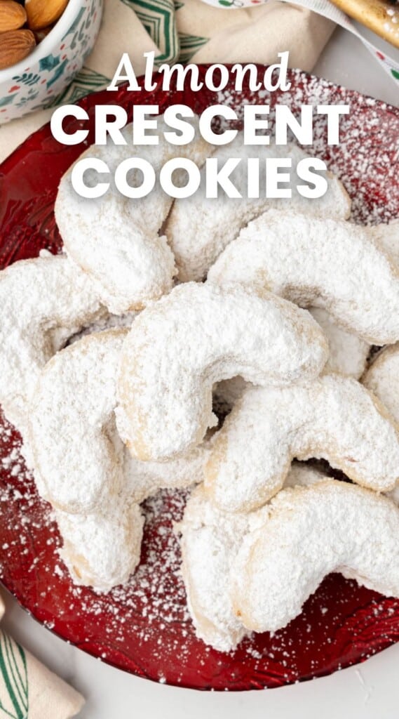 a red plate of crescent shaped almond cookies coated in powdered sugar. Text overlay says "almond crescent cookies" in white lettering.