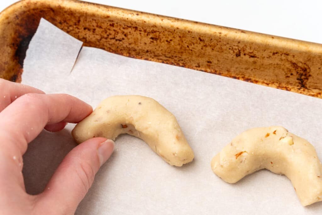 a hand placing almond crescents on a parchment lined pan before baking.