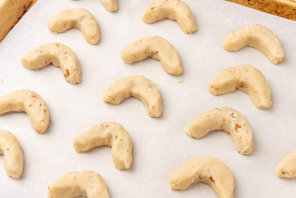 three rows of almond crescents on a parchment lined baking sheet, ready to be baked.