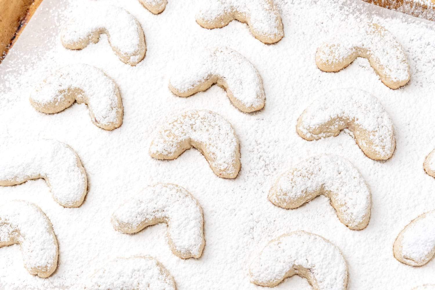 Powdered sugar has been dusted over almond crescent cookies on a sheet pan.