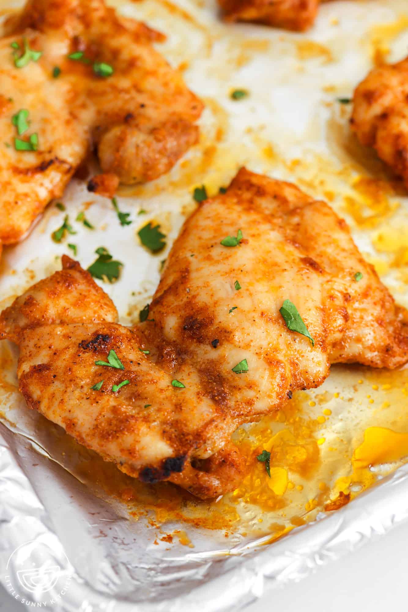 a foil lined baking sheet with baked, seasoned chicken thighs.