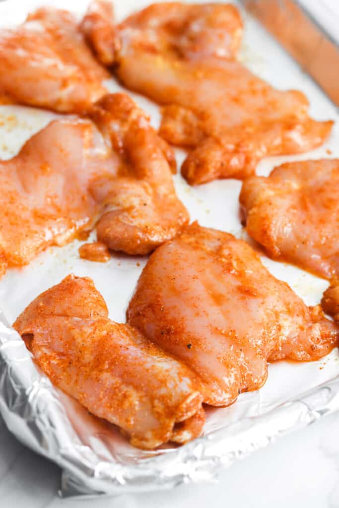 raw boneless skinless chicken thighs seasoned and placed on foil.