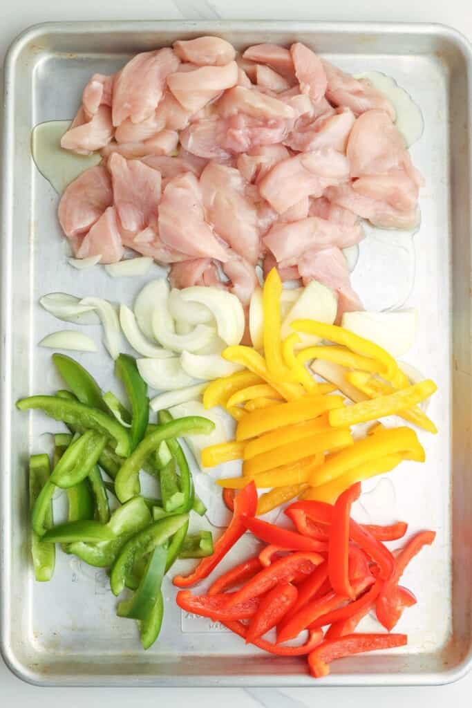 sliced chicken breast and vegetables on a sheet pan.