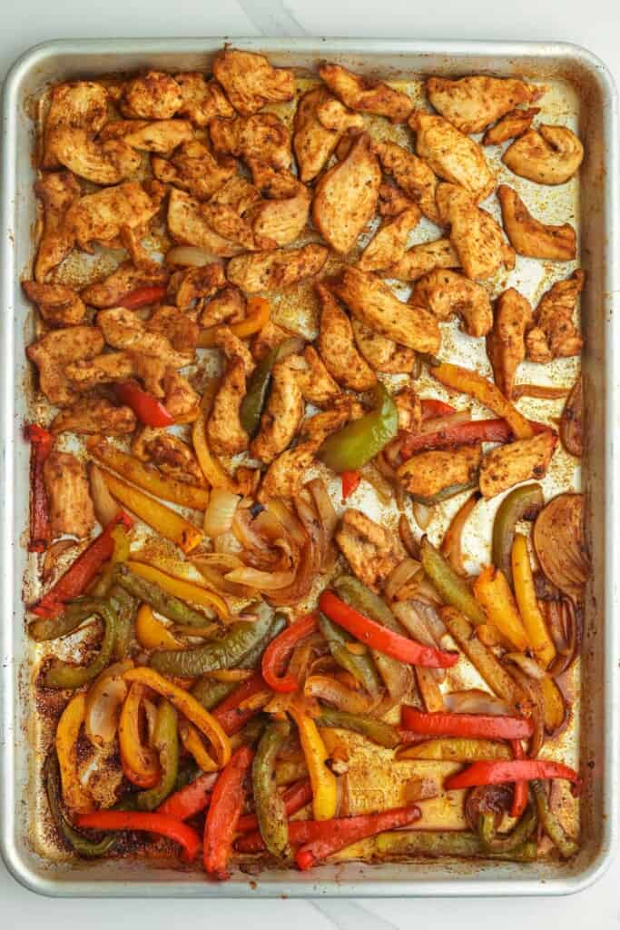 cooked chicken strips, peppers, and onions on a sheet pan.