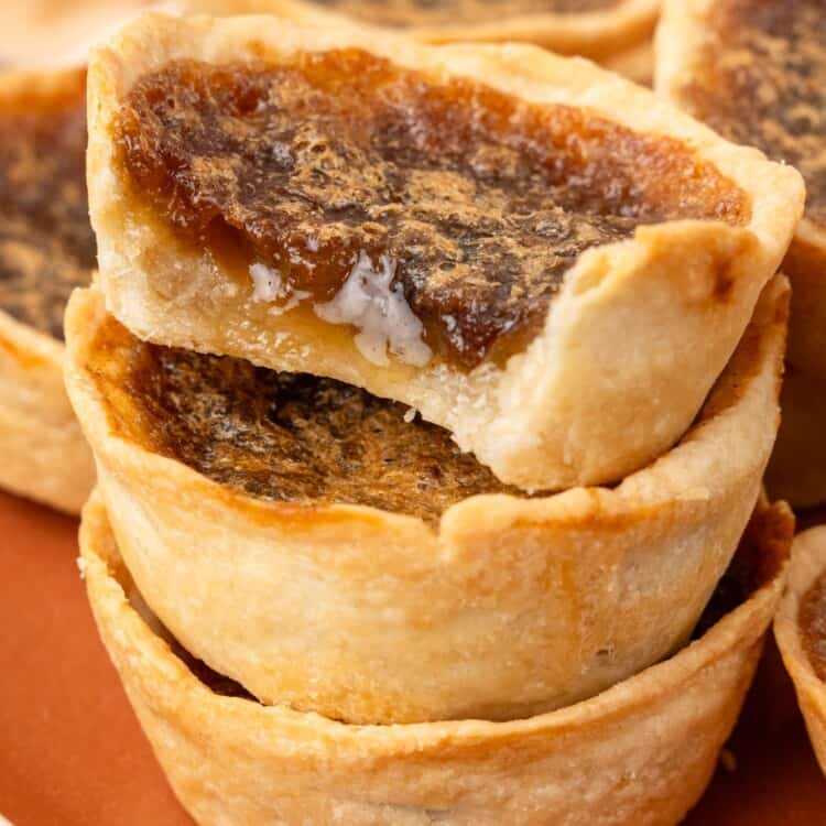 a plate of flaky butter tarts. one has a bite taken to show the sugary filling.