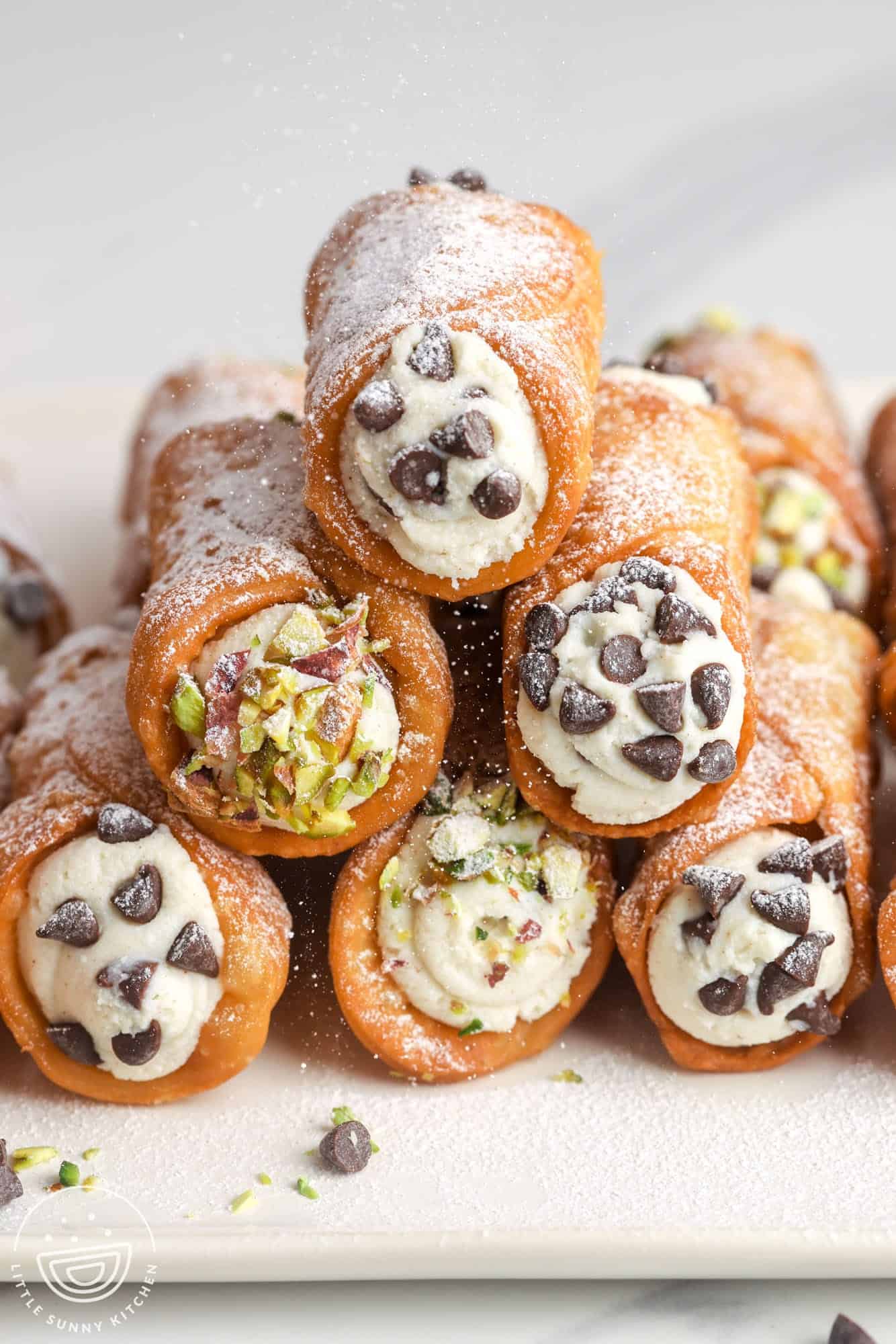 a stack of finished cannoli with the ends dipped in chocolate chips and chopped nuts. 