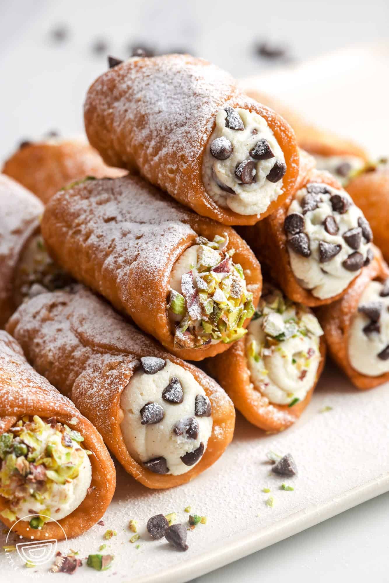 7 cannoli stacked into a pyramid. Some are dipped in chopped pistachios, some into mini chocolate chips. 